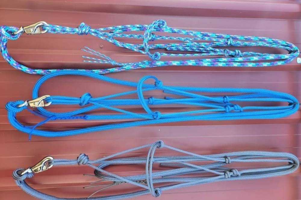 Three handcrafted rope halters with metal clips neatly laid out on a corrugated metal surface-